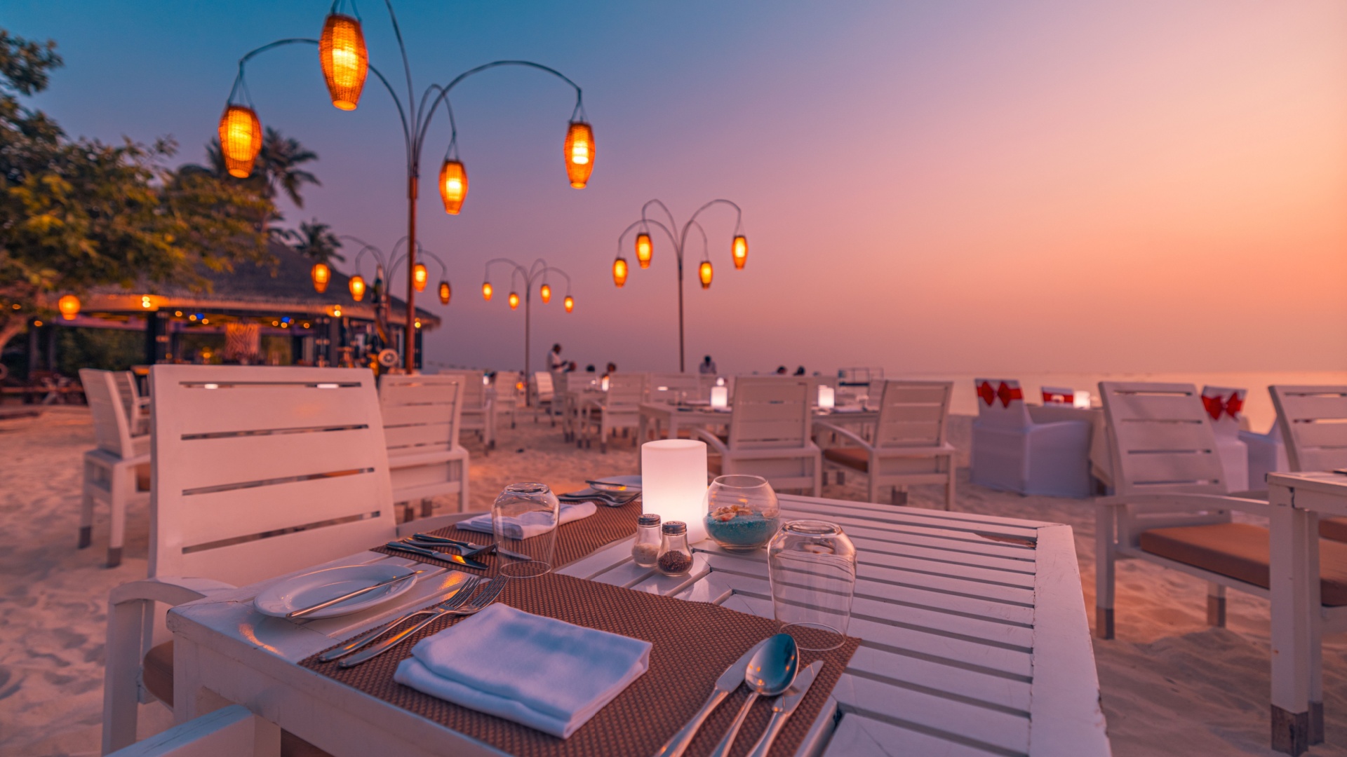 Open-air beachside dining pavilion at a tropical resort, tables set for an evening meal